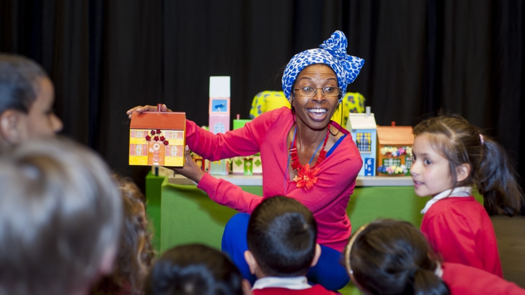 A speaker holding a small model of a house to show primary school children.