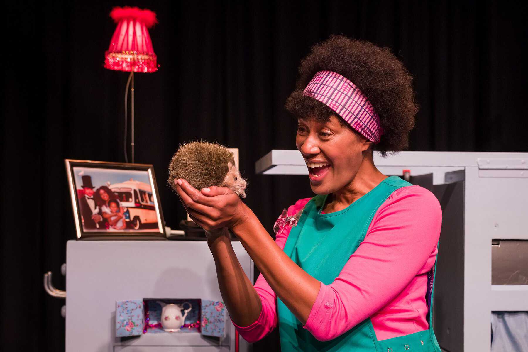 A performer on stage holding a prop of a fake hedgehog and smiling happily.