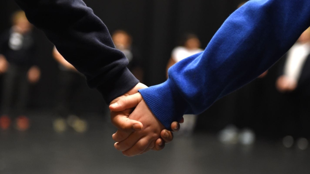 A close up of 2 children holding hands.