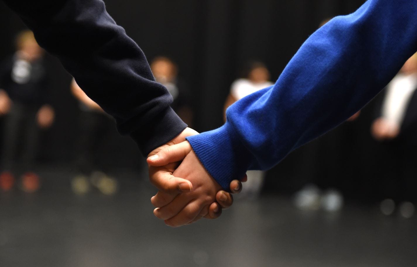 A close up of 2 children holding hands.