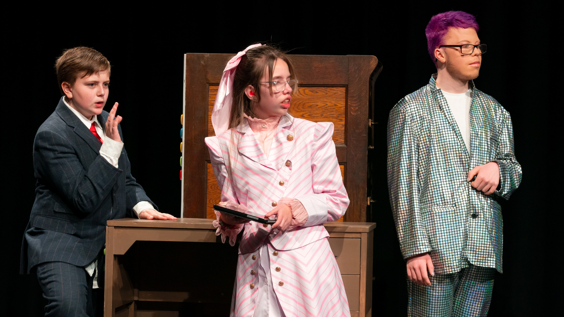 A group of young performers in formal dress stood in front of a wooden desk.