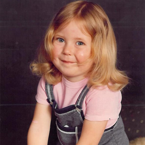 A medium close up image of a very young Joss Matzen smiling at the camera in grey dungarees.