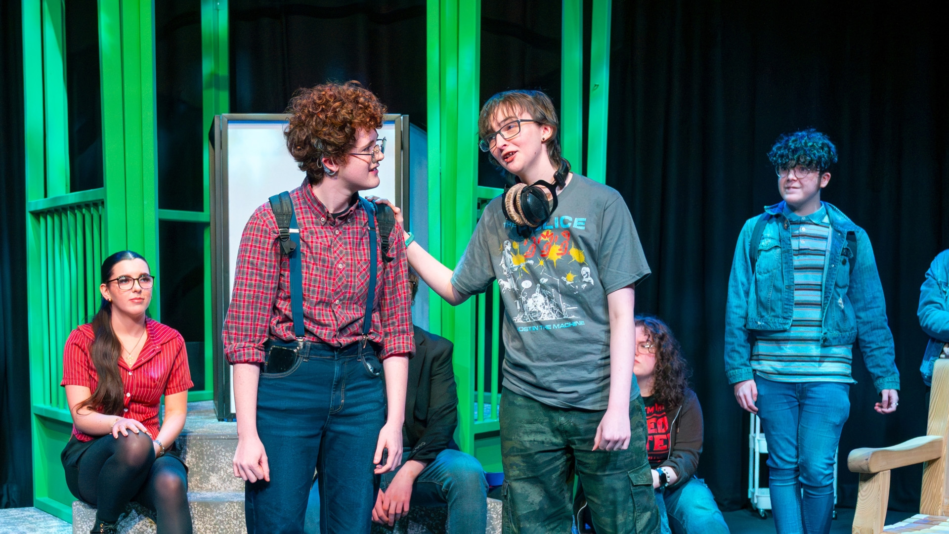 A group of young performers on stage mid dialogue.