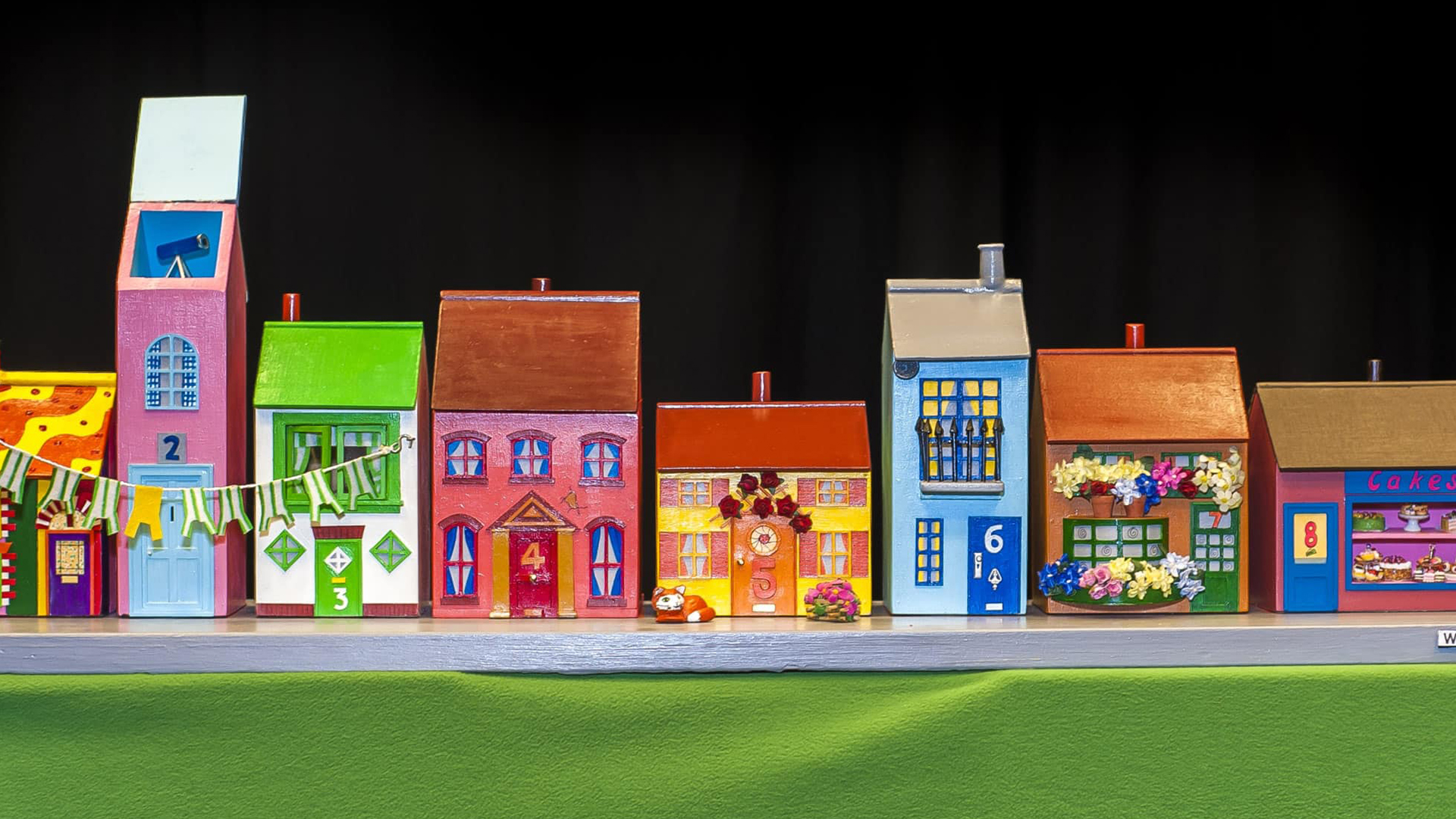 A row of 8 model houses in a variety of bright colours. The house numbers from left to right are: 2, 3, 4, 5, 6, 7, 8.