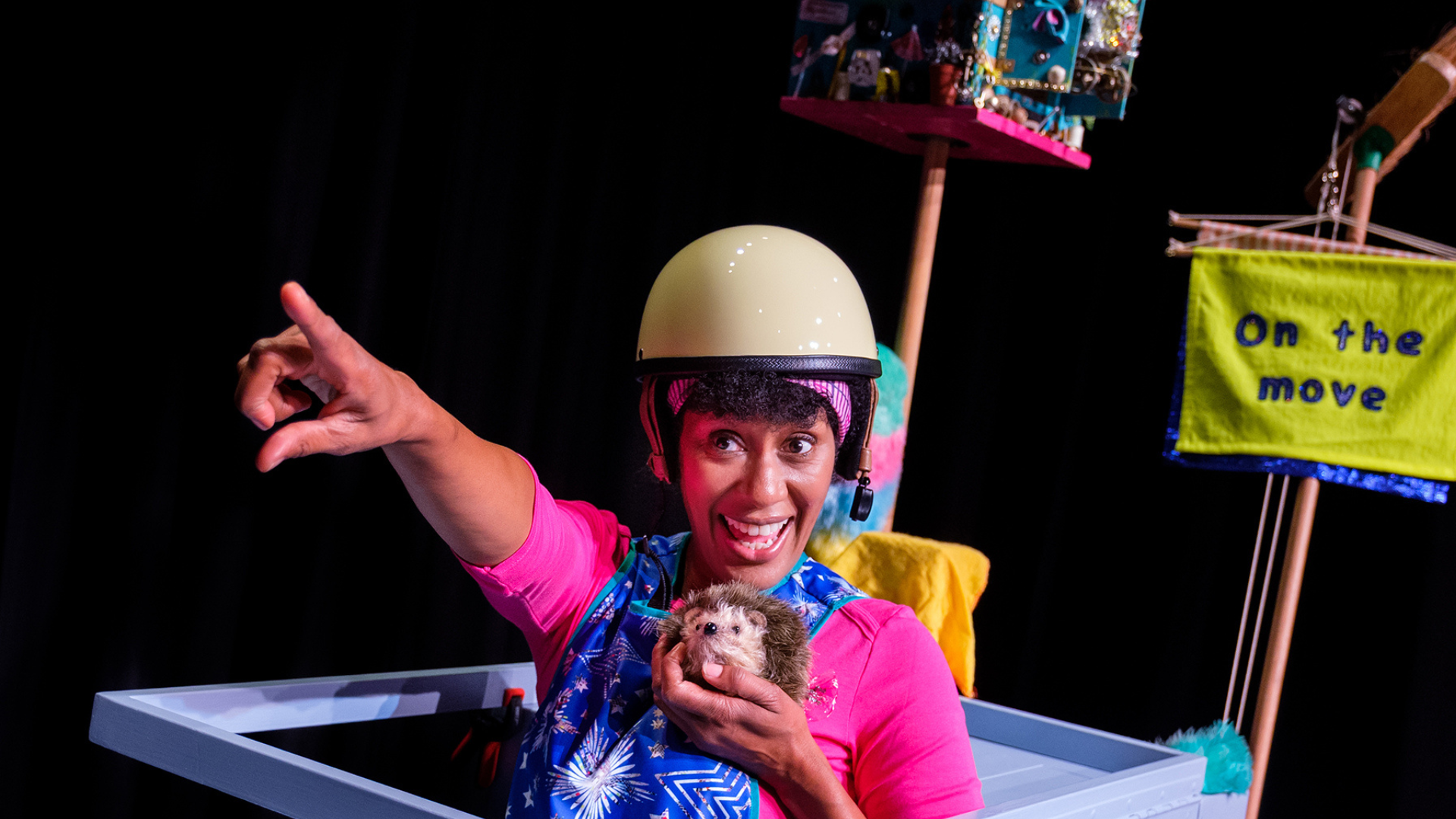 A close up of a performer in a bike helmet holding a prop hedgehog in their hands.
