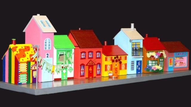 A row of 8 model houses in a variety of bright colours. The house numbers from left to right are: 1, 2, 3, 4, 5, 6, 7, 8.
